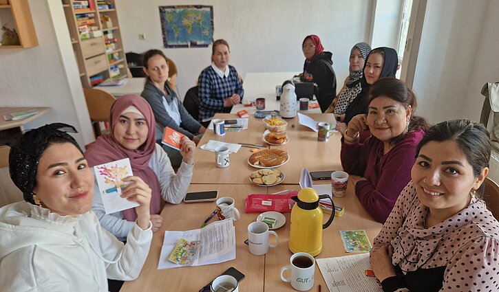 Auf dem Bild zu sehen sind eine Gruppe von Migrantinnen, die im Deutschkurs um einen Tischsitzen.