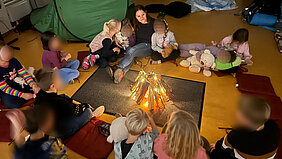 Schulkinder der Adventschule Oberhavel sitzem bei Kerzenlicht im Kreis und hören zu, wie ihnen vorgelesen wird.