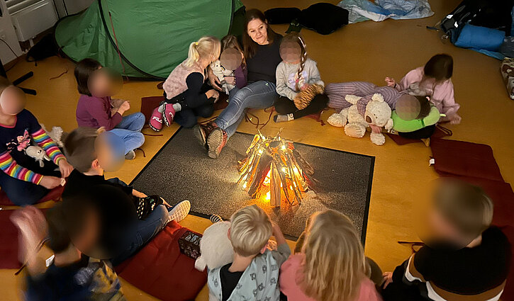 Schulkinder der Adventschule Oberhavel sitzem bei Kerzenlicht im Kreis und hören zu, wie ihnen vorgelesen wird.