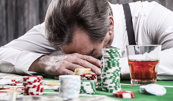 Das Bild zeigt einen Mann hinter einem Spieltisch, den Kopf in den Händen haltend